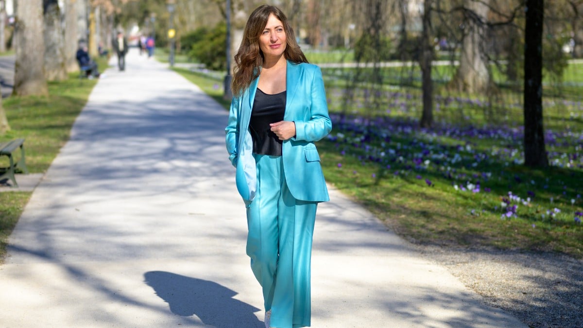 Woman styling turquoise pants with a black top and matching blazer outdoors.