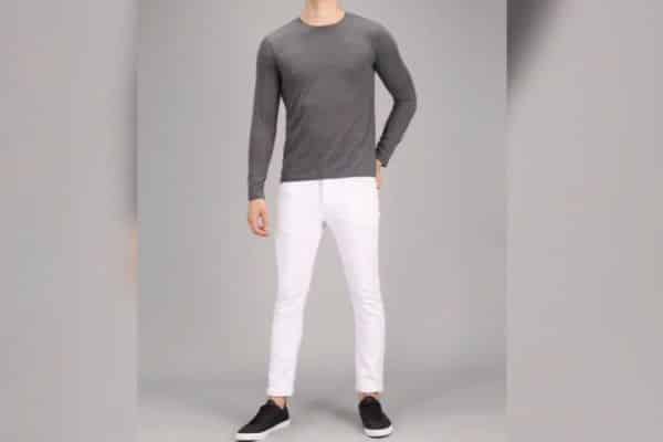 Man wearing a fitted grey long-sleeve shirt with slim white pants and sneakers, showcasing a clean, modern casual outfit.