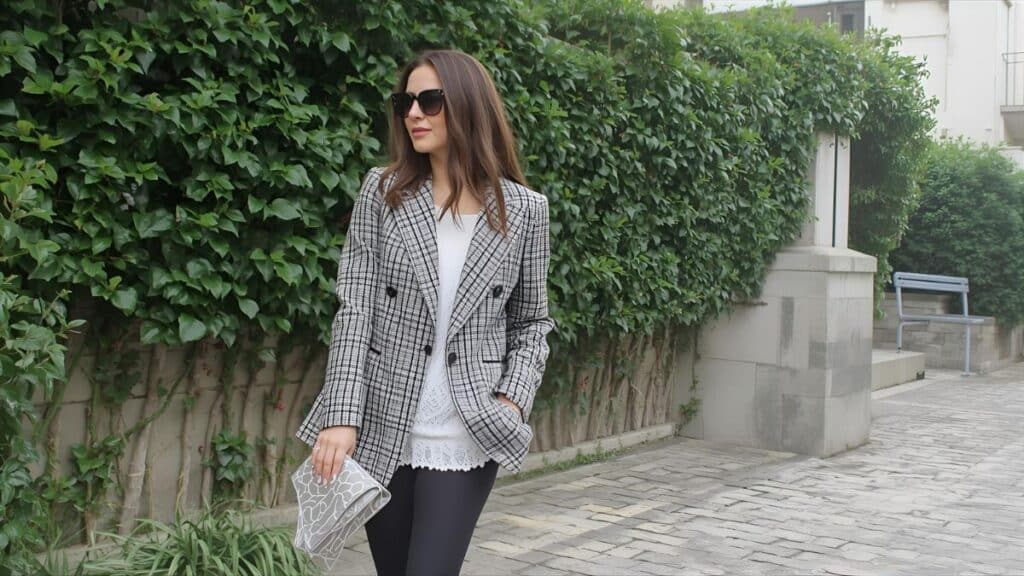 A stylish woman demonstrating what to wear with a blazer female, pairing a grey plaid blazer with a white top, black pants, and a clutch while walking outdoors.