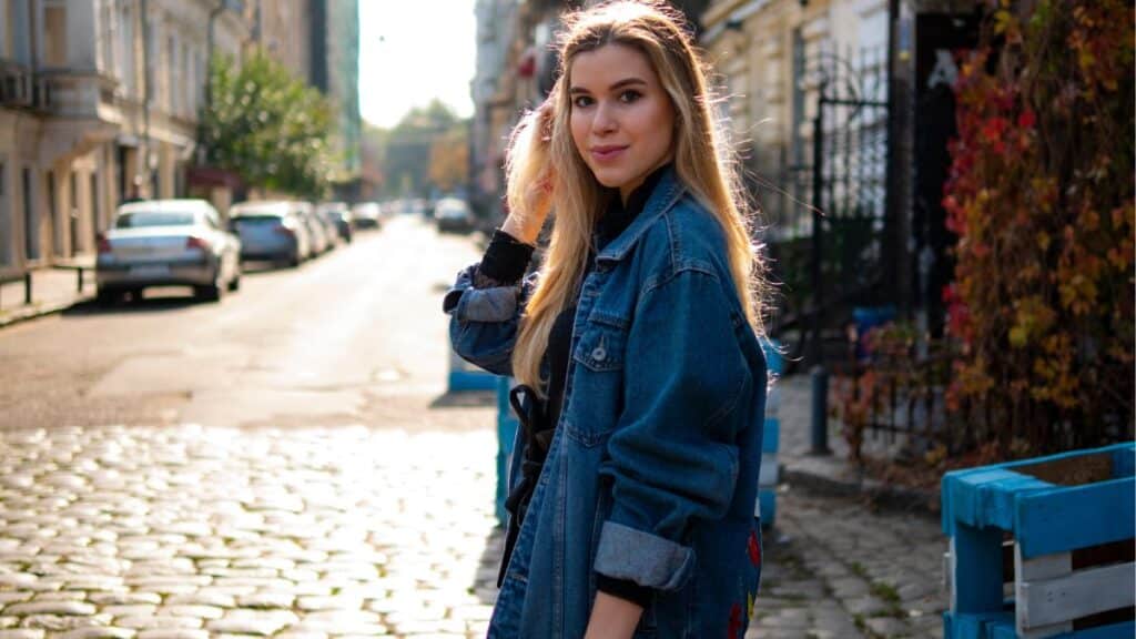 Stylish woman in a boxy denim jacket walking in an old alley, demonstrating how to style a boxy denim jacket