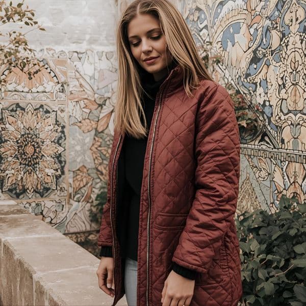 A woman wearing a maroon quilted jacket styled with a black top and light jeans, showing a modern example for the question “Are quilted jackets still in style” in everyday fashion.