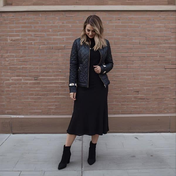 Woman wearing a black quilted jacket styled over a black midi dress with ankle boots, showing how to style quilted jackets over dresses in a chic fall outfit.